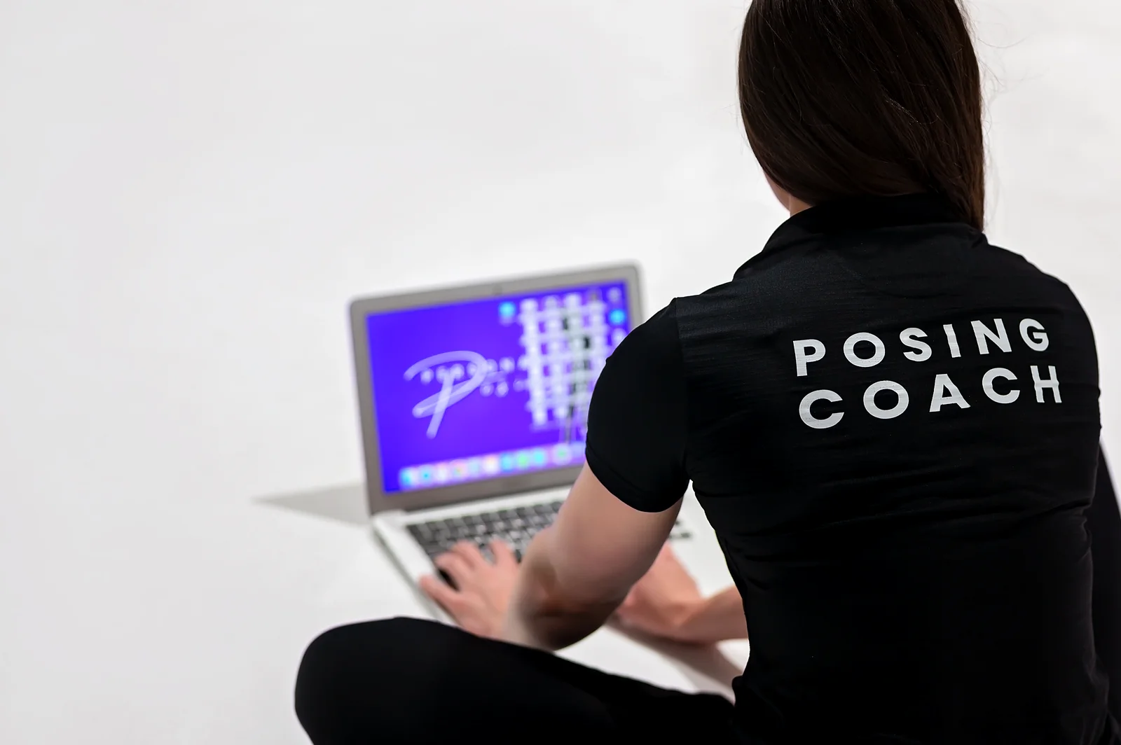 Georgia at her laptop in a POSING COACH shirt, running an online session